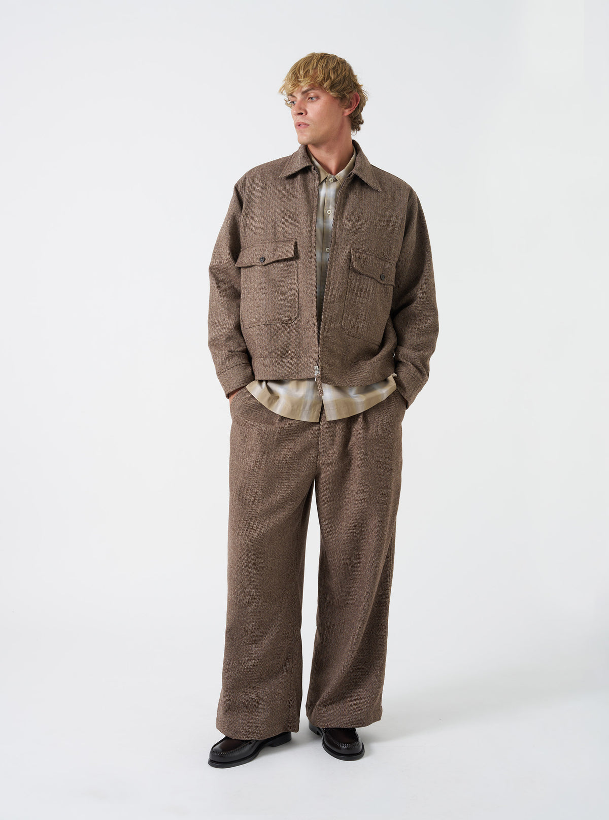 A front view of a model wearing the Brown Wool Herringbone E130 Jacket. The brown jacket features a textured herringbone wool weave, full front button placket, classic collar, and lower side pockets against a plain background.