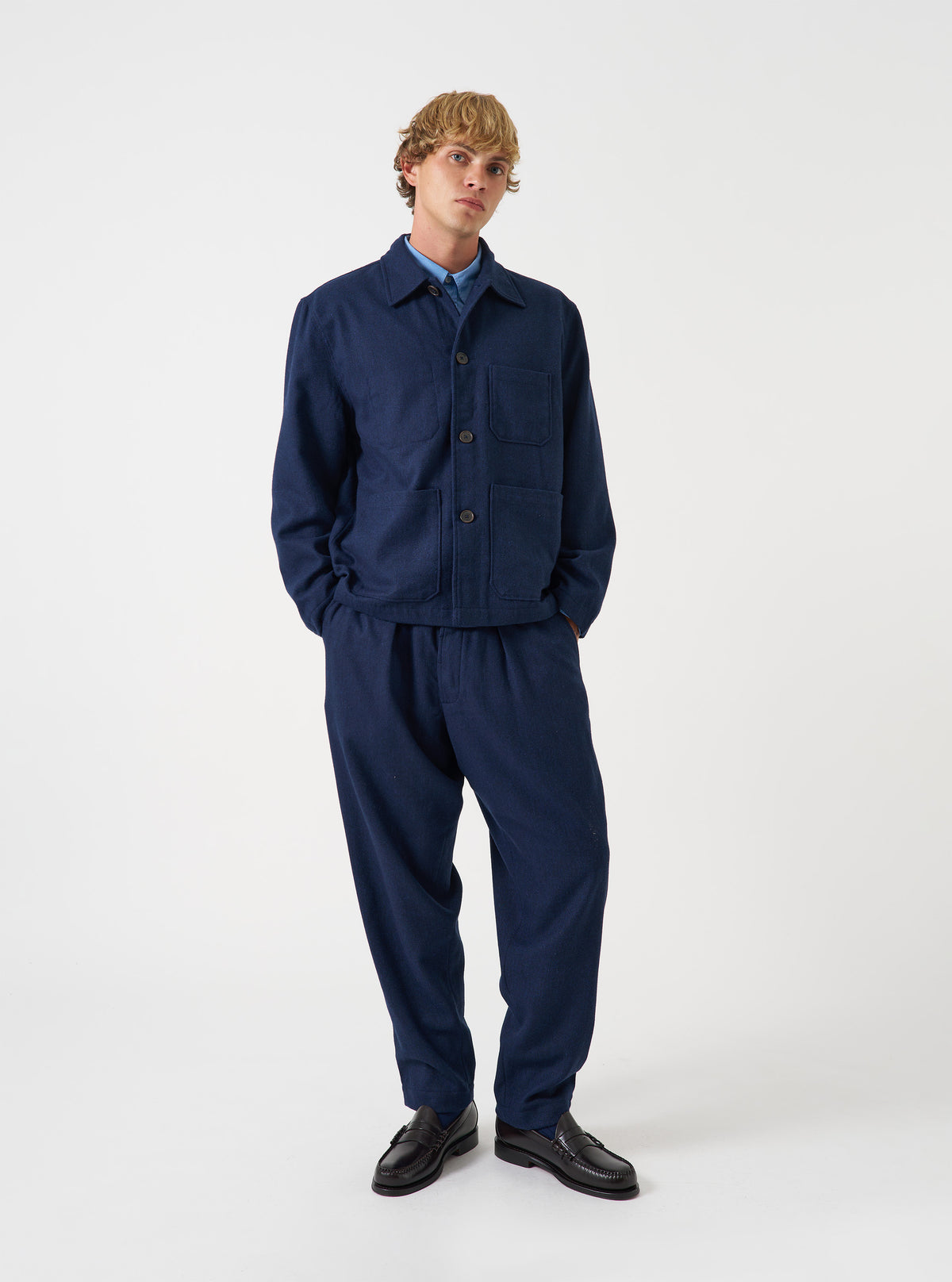 A front view of a model wearing the Navy Wool Herringbone Ives Jacket. The navy blue chore jacket shows front button closures, structured collar, and prominent patch pockets made from wool herringbone against a plain backdrop.