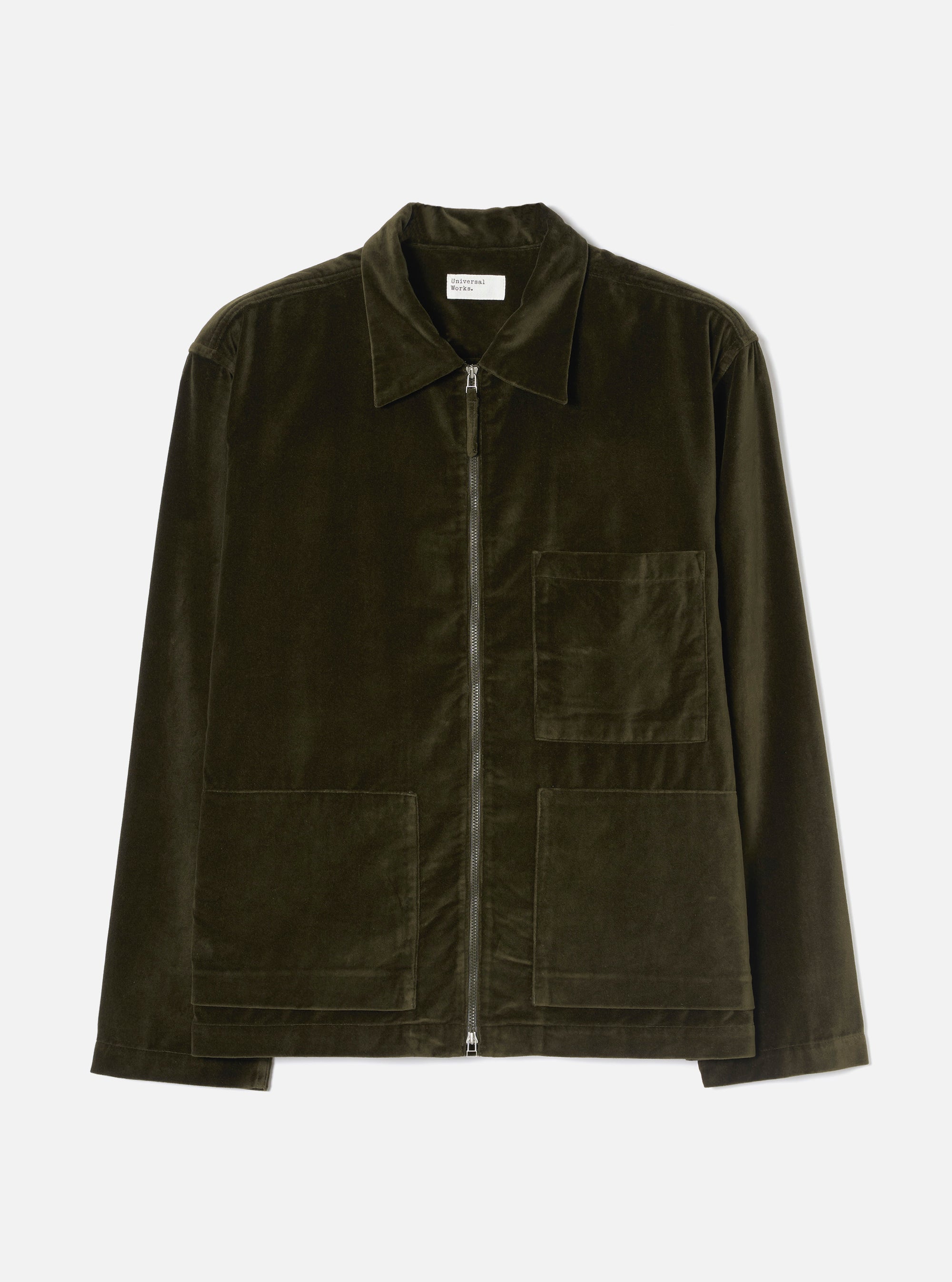Olive velvet zip-through overshirt laid flat on a light grey studio backdrop. Features a point collar, full-length silver zip, one chest patch pocket, two large lower patch pockets, and plain cuffs. The soft velvet fabric has a subtle sheen. A Universal Works woven label sits at the collar.