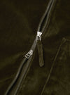 Close-up of the centre-front zip on an olive velvet zip shirt. A two-way silver-tone zip runs diagonally across the frame, with both the upper and lower sliders visible. The top slider has a suede fabric pull tab. The soft, napped velvet texture of the olive fabric fills the background.