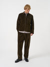 A model wearing the Universal Works Olive CPH Velvet Oxford Pant, shown from the front. The olive green cotton velvet trousers feature a comfortable drawstring waist, front pleats, and wide legs against a plain background.