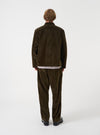 A back view of a model wearing the Universal Works Olive CPH Velvet Oxford Pant. The image highlights the relaxed fit of the olive green cotton velvet trousers, showing the straight hem and back pocket detail against a neutral backdrop.