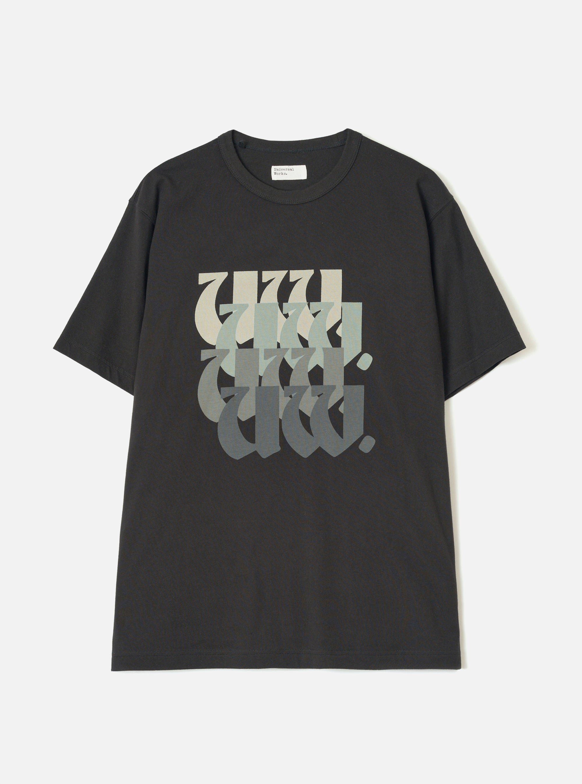 Black single jersey t-shirt laid flat on a white studio surface. Crew neck with a small Universal Works woven label at the back neck. Short sleeves with a relaxed fit. Large chest graphic featuring stacked "UW" lettering in a blackletter style, fading from cream through sage green to dark grey.