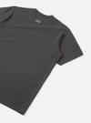 Flat lay of a black single jersey t-shirt shot from behind on a light grey seamless backdrop. The back panel is plain with a small tonal UW logo print near the neckline. Smooth jersey fabric with a clean crew neck and short sleeves with hemmed cuffs visible.
