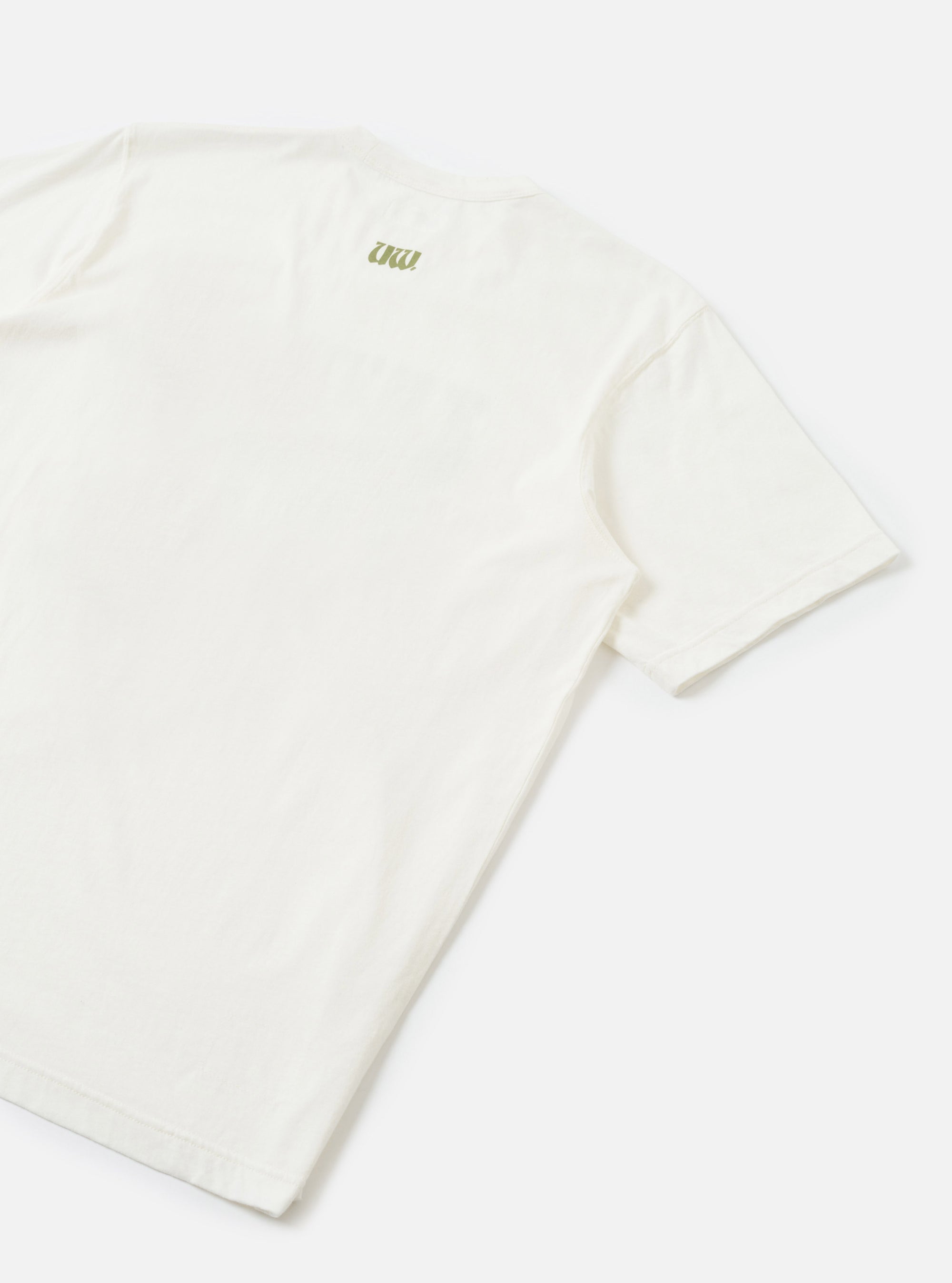 Flat lay of an ecru single jersey t-shirt, shot from above at an angle showing the back. A small olive green branded logo print sits at the upper back centre. Short sleeves with ribbed cuffs are visible. The fabric has a smooth, fine jersey texture. Plain white studio surface.