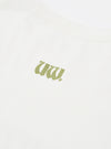Close-up flat lay of an ecru single jersey t-shirt. A small olive green gothic-style logo print sits at centre chest. The cotton fabric texture is visible. A seam is partially visible at the top of the frame. Plain white surface background.