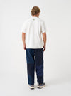 A rear view of a model wearing the Universal Works Ecru Single Jersey UW Print Core Tee. The photo highlights the relaxed silhouette and neat stitching of the cream-coloured cotton jersey t-shirt set against a plain background.