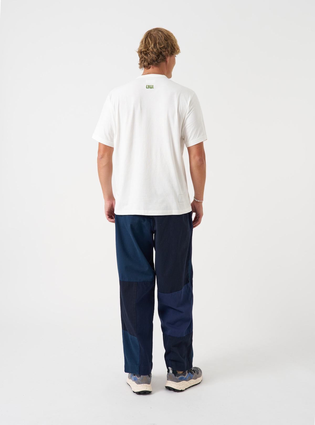 A rear view of a model wearing the Universal Works Ecru Single Jersey UW Print Core Tee. The photo highlights the relaxed silhouette and neat stitching of the cream-coloured cotton jersey t-shirt set against a plain background.