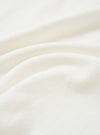 Close-up of the ecru single jersey fabric used in the Core Tee, showing a soft, fine knit texture with natural drape and gentle folds across the frame. The off-white tone is consistent throughout. No garment details or model are visible.
