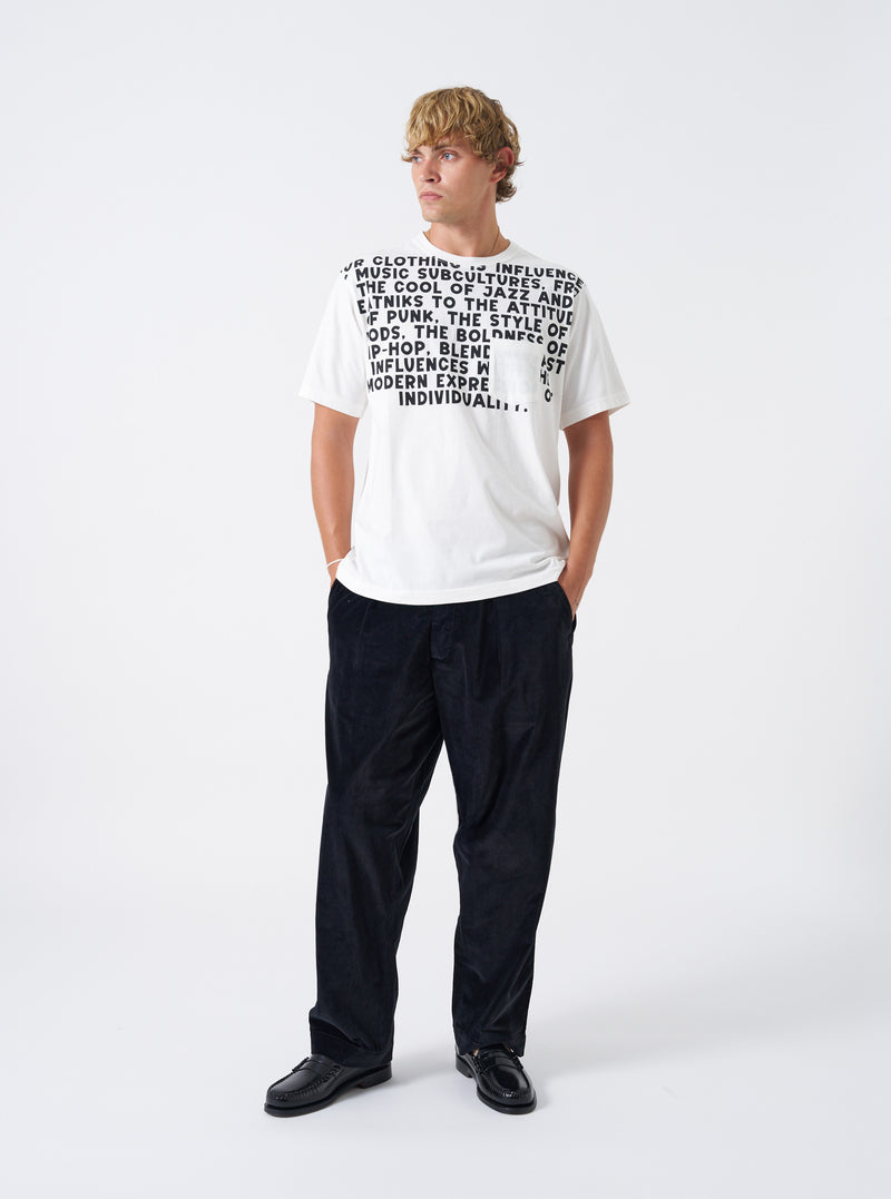A model wearing the Universal Works Ecru Single Jersey Jazz Cool Of Jazz Core Pocket Tee, captured from the front. The light ecru short-sleeve t-shirt shows a chest pocket graphic, crew neck, and cotton finish against a plain backdrop.