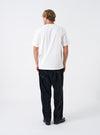 A back view of a model wearing the Universal Works Ecru Single Jersey Jazz Cool Of Jazz Core Pocket Tee. The photograph displays the clean rear fit and lightweight cotton jersey fabric of the ecru t-shirt against a plain backdrop.