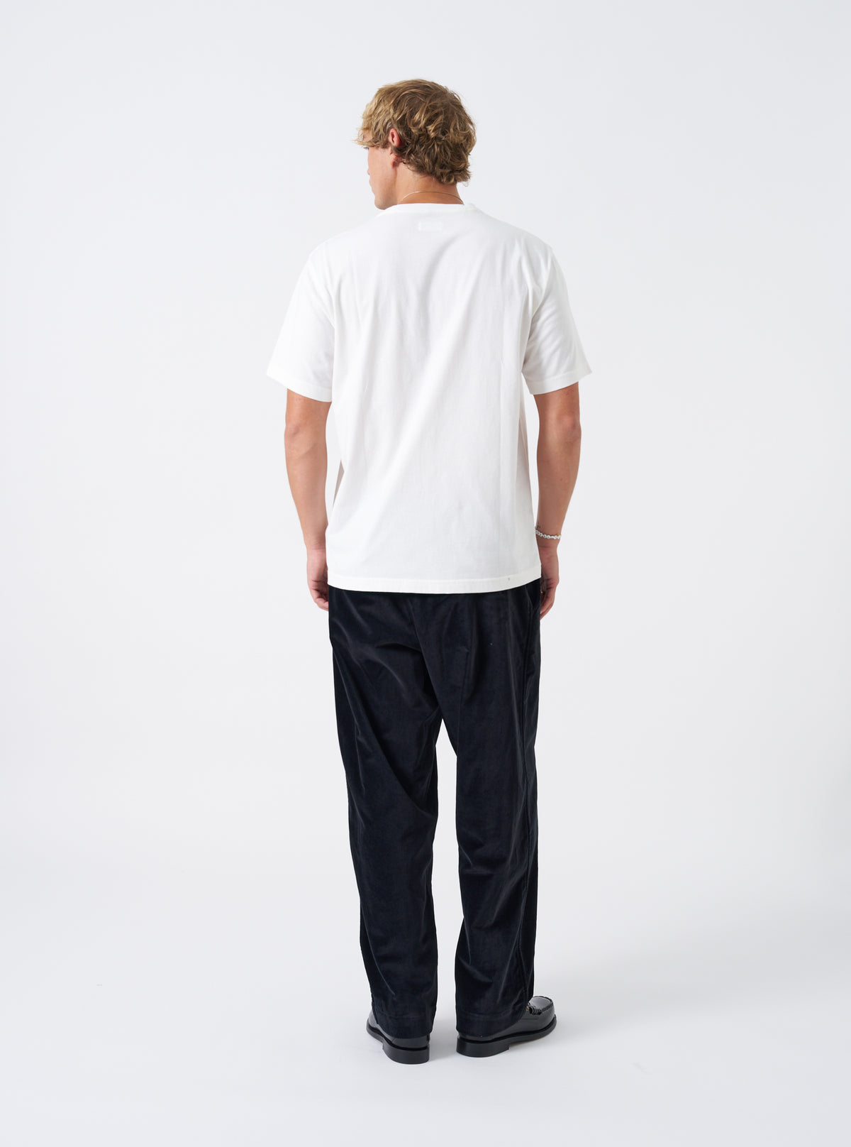 A back view of a model wearing the Universal Works Ecru Single Jersey Jazz Cool Of Jazz Core Pocket Tee. The photograph displays the clean rear fit and lightweight cotton jersey fabric of the ecru t-shirt against a plain backdrop.