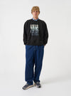 A model wearing the Universal Works Black Brush Back Sweat UW UW Print Raglan Sweatshirt, shown from the front. The black cotton sweatshirt features raglan sleeves, ribbed cuffs, crew neck, and graphic print against a plain backdrop.