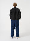A rear view of a model wearing the Universal Works Black Brush Back Sweat UW UW Print Raglan Sweatshirt. The image highlights the raglan sleeve seams, ribbed hemline, and relaxed back fit of the black sweatshirt on a plain background.