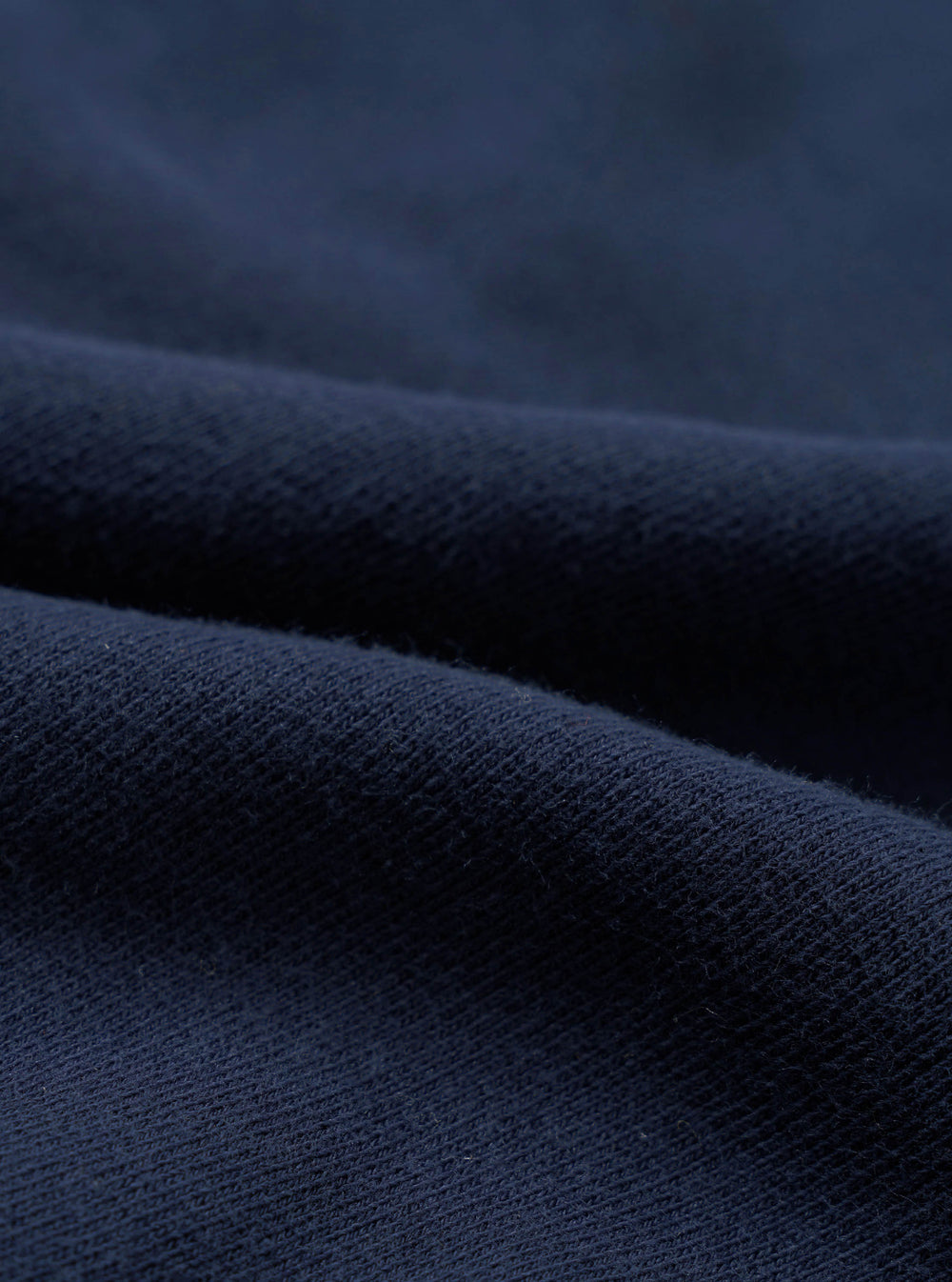 Close-up detail shot of navy brushback fleece fabric, showing a soft, dense looped texture on the reverse side and a smooth face. The material is folded to reveal both surfaces, highlighting the fabric's weight and finish.