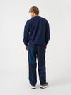 A back view of a model wearing the Universal Works Navy Brushback Sweat Cool Of Jazz Loose Sweatshirt. The shot highlights the loose silhouette, raglan shoulders, and deep navy shade of the cotton sweatshirt against a plain backdrop.