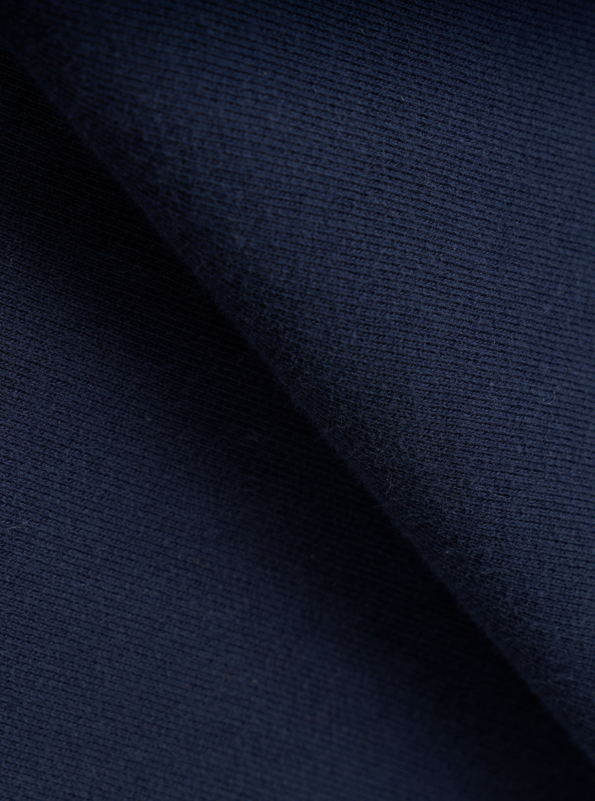 A macro swatch photograph showing the detailed fabric texture of the Universal Works Navy Brushback Sweat Cool Of Jazz Loose Sweatshirt. The close up highlights the deep navy blue tone and soft brushed cotton weave of the garment.