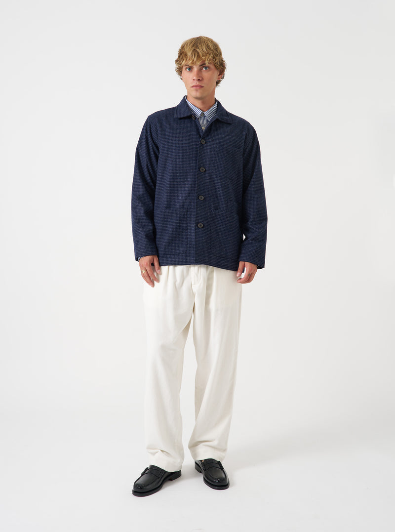 A front view of a model wearing the Universal Works Navy Check Bobby Wool Mix Bakers Overshirt. The dark blue check overshirt features a button front fastening, classic collar, chest pocket, and lower patch pockets against a plain neutral background.