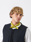 A styled shot featuring multiple neckerchiefs including the Light Olive Jazz/Beatniks Print Neckerchief on a neutral background, displaying its subtle olive shade and printed graphic text.