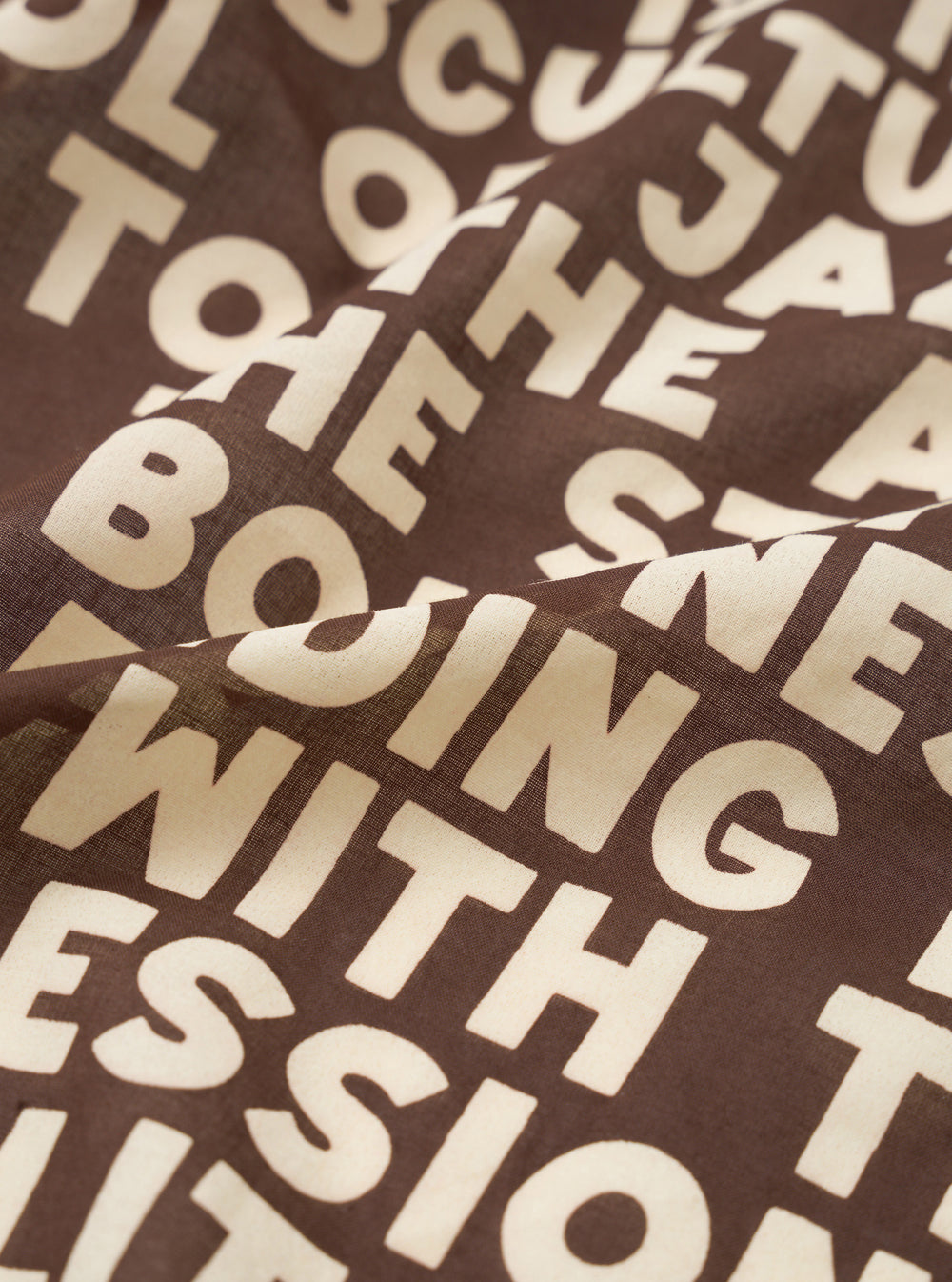 A close-up fabric swatch view of the Brown Jazz/Beatniks Print Neckerchief on a solid backdrop, showing the detailed text graphic design and the texture of the soft cotton material.