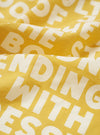 A close-up swatch image of the Mustard Jazz/Beatniks Print Neckerchief on a plain background, highlighting the mustard yellow cotton fabric and detailed jazz graphic text pattern.