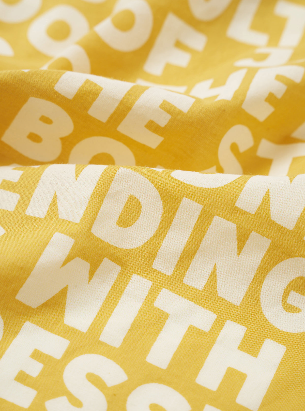A close-up swatch image of the Mustard Jazz/Beatniks Print Neckerchief on a plain background, highlighting the mustard yellow cotton fabric and detailed jazz graphic text pattern.
