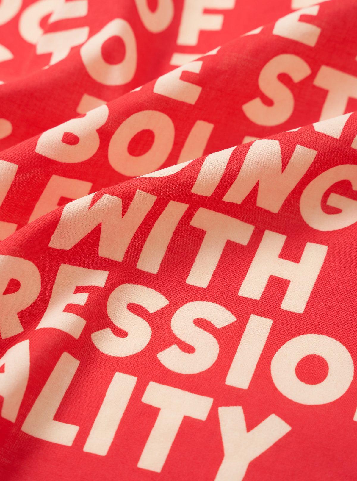 A close-up fabric swatch of the Red Jazz/Beatniks Print Neckerchief against a solid background, showcasing the bright red cotton texture and intricate graphic print typography.