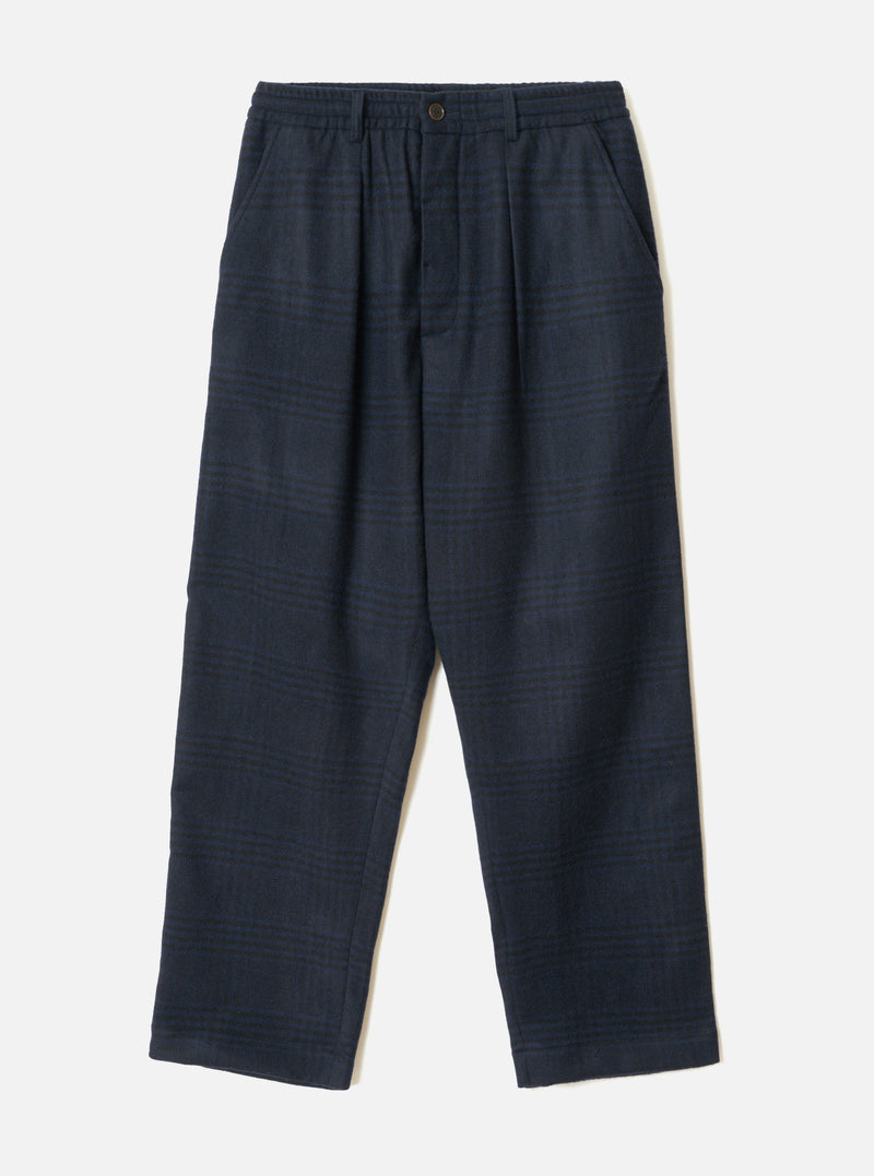 The Navy Bob Wool Mix Oxford Pant is laid flat on a light grey backdrop. It features a dark blue glen plaid pattern, elasticated waistband with a central metal button, twin front pleats, slant side pockets, and wide straight legs with plain hems.