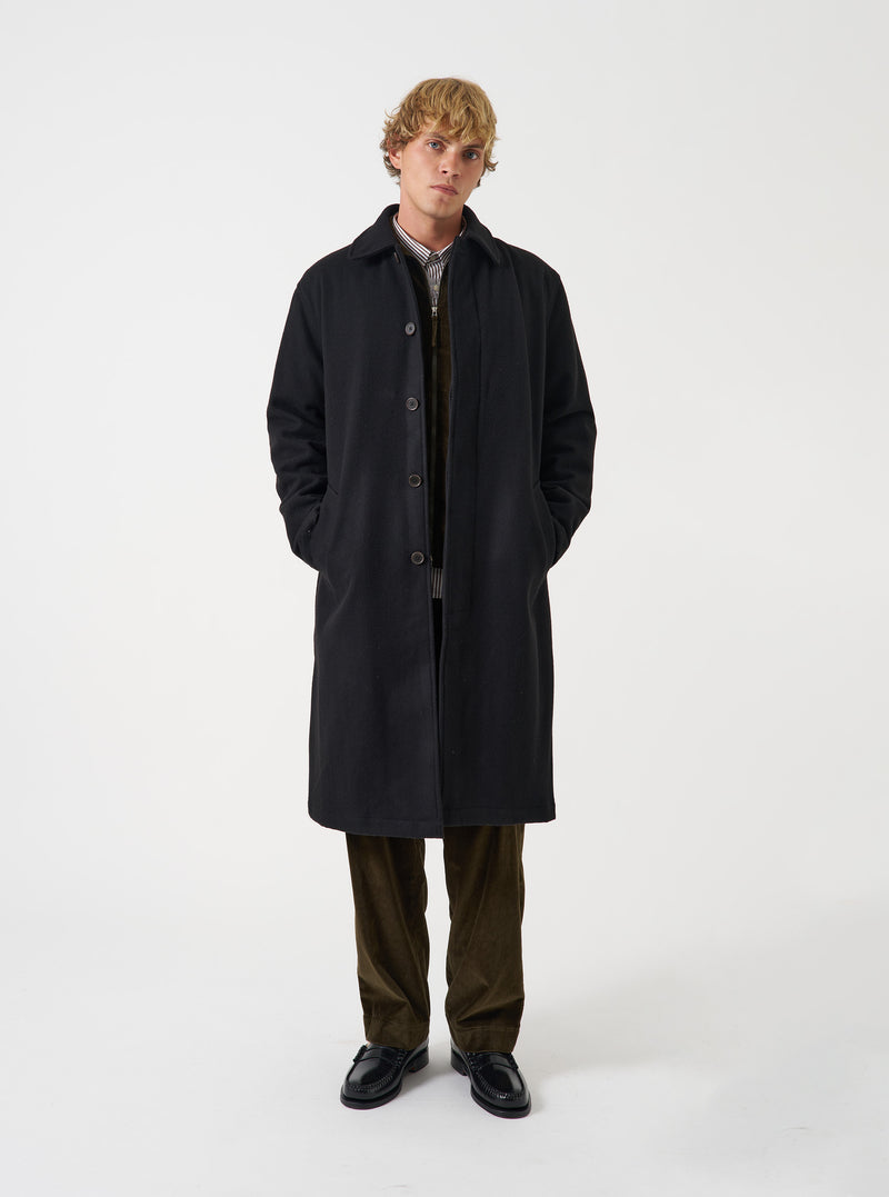 A model wearing the Black Mowbray Mac Coat against a plain studio background. The classic mac coat features a clean front closure, structured collar, and warm wool-blend construction.