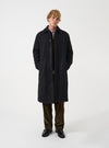 A model wearing the Black Mowbray Mac Coat against a plain studio background. The classic mac coat features a clean front closure, structured collar, and warm wool-blend construction.