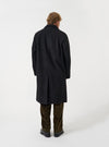 An alternative view of a model wearing the Black Mowbray Mac Coat on a neutral backdrop, highlighting the longline silhouette, classic collar detail, and tailored dark grey-black fit.