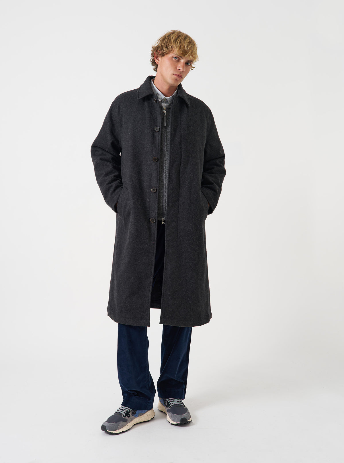 A model wearing the Grey Marl Mowbray Mac Coat against a plain studio background. The long mac coat features a classic collar, front button fastening, welt pockets, and a straight, loose fit.