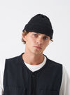 A model wearing the Black British Wool Short Watch Cap against a clean studio background. The short beanie sits close above the ears and features a turned-up cuff and a pinched crown profile.