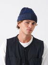 A model wearing the Navy British Wool Short Watch Cap against a plain studio backdrop. The dark navy knitted beanie sits snugly on the head, highlighting its compact shape and classic ribbed cuff.