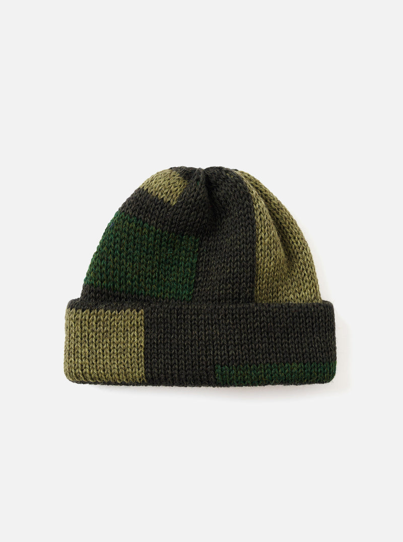 The Patched Olive British Wool Short Watch Cap presented flat against a neutral light background. This olive green knitted hat features a short beanie silhouette with a distinctive fabric patch detail.