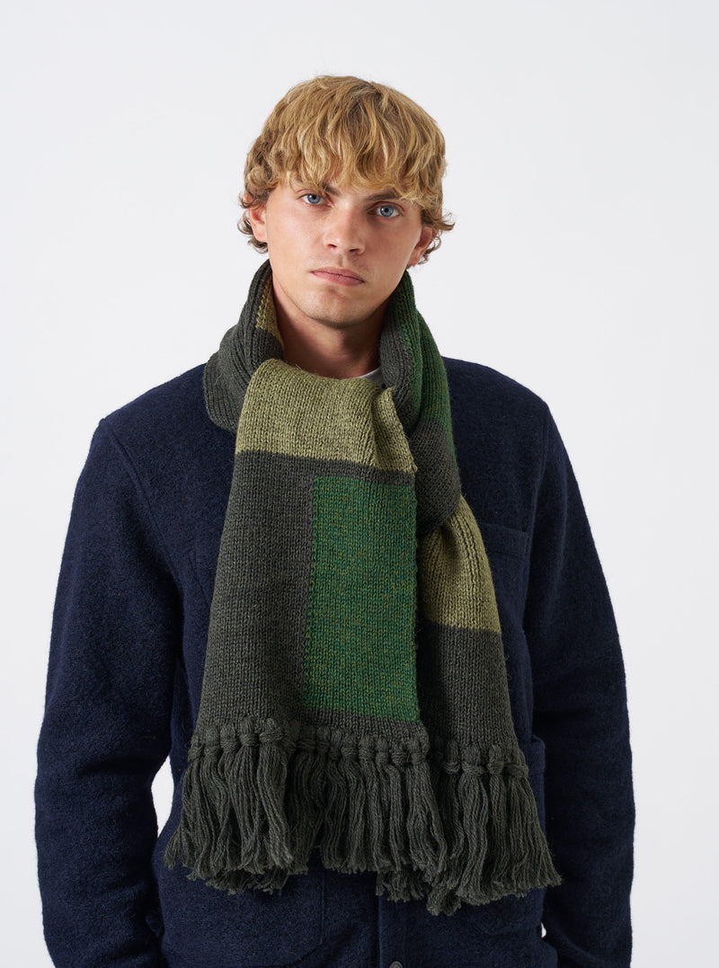 A model wearing the Olive British Wool Scarf styled around the shoulders against a neutral backdrop. The olive green scarf showcases its soft drape, full length, and classic British wool texture.