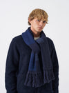 A model wearing the Navy British Wool Scarf wrapped styled around the neck against a plain background. The dark navy wool scarf displays its full length, soft drape, and textured ribbed knit ends.
