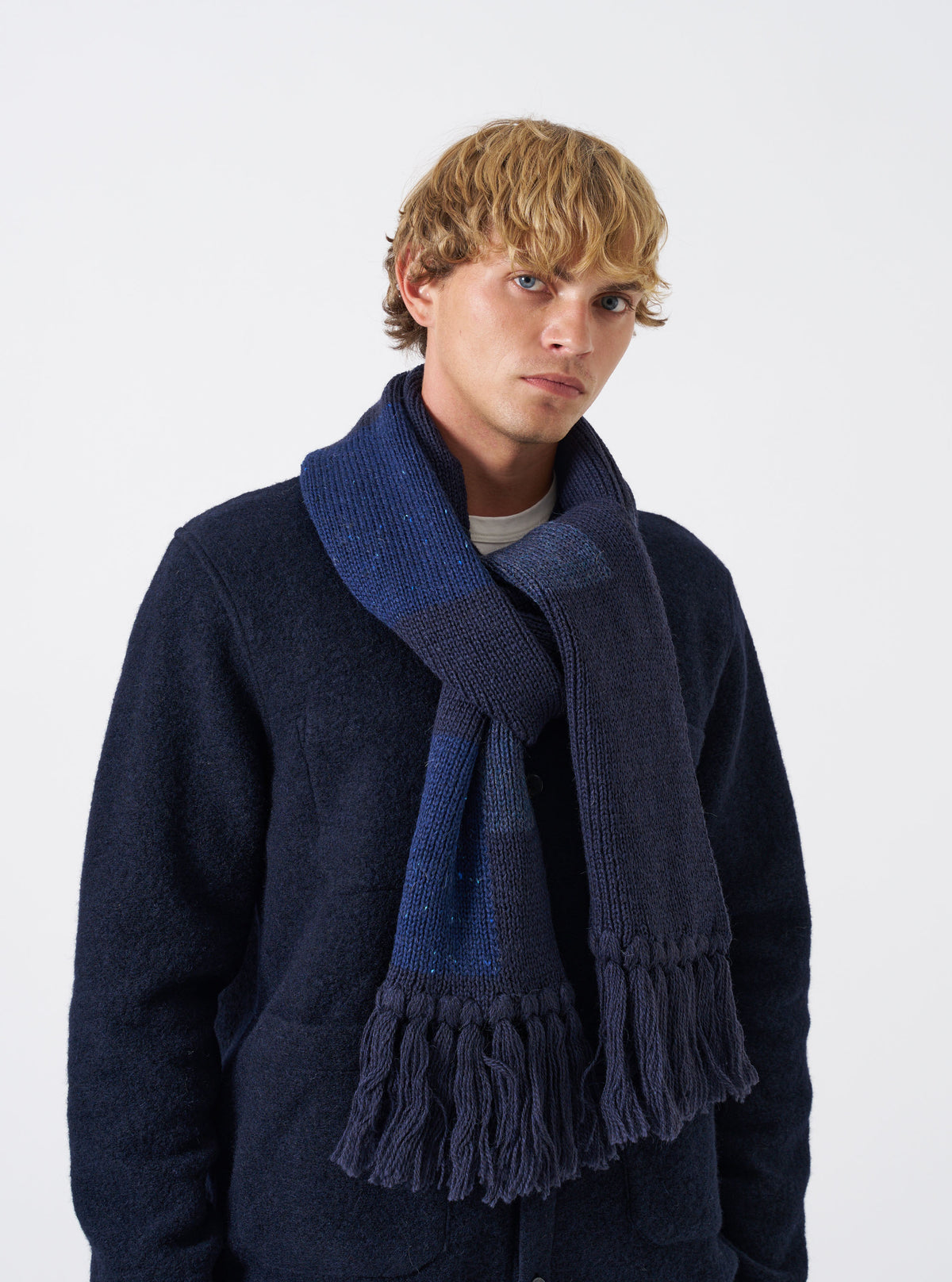 A model wearing the Navy British Wool Scarf wrapped styled around the neck against a plain background. The dark navy wool scarf displays its full length, soft drape, and textured ribbed knit ends.