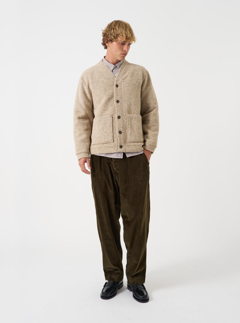 A model wearing the Fawn Wool Fleece Advance Cardigan against a plain studio background. The V-neck cardigan is buttoned up, showing its loose boxy silhouette, fawn beige color, and front patch pockets.