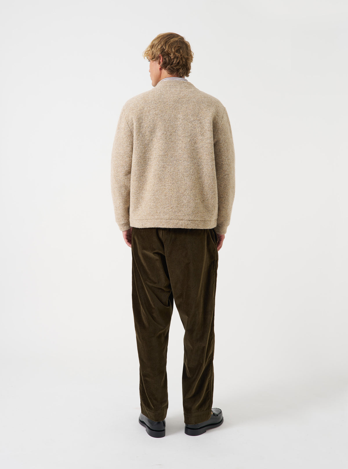 A model wearing the Fawn Wool Fleece Advance Cardigan captured from an alternate angle against a plain studio background, highlighting the casual fit, soft drape, and neutral fawn wool fleece texture.