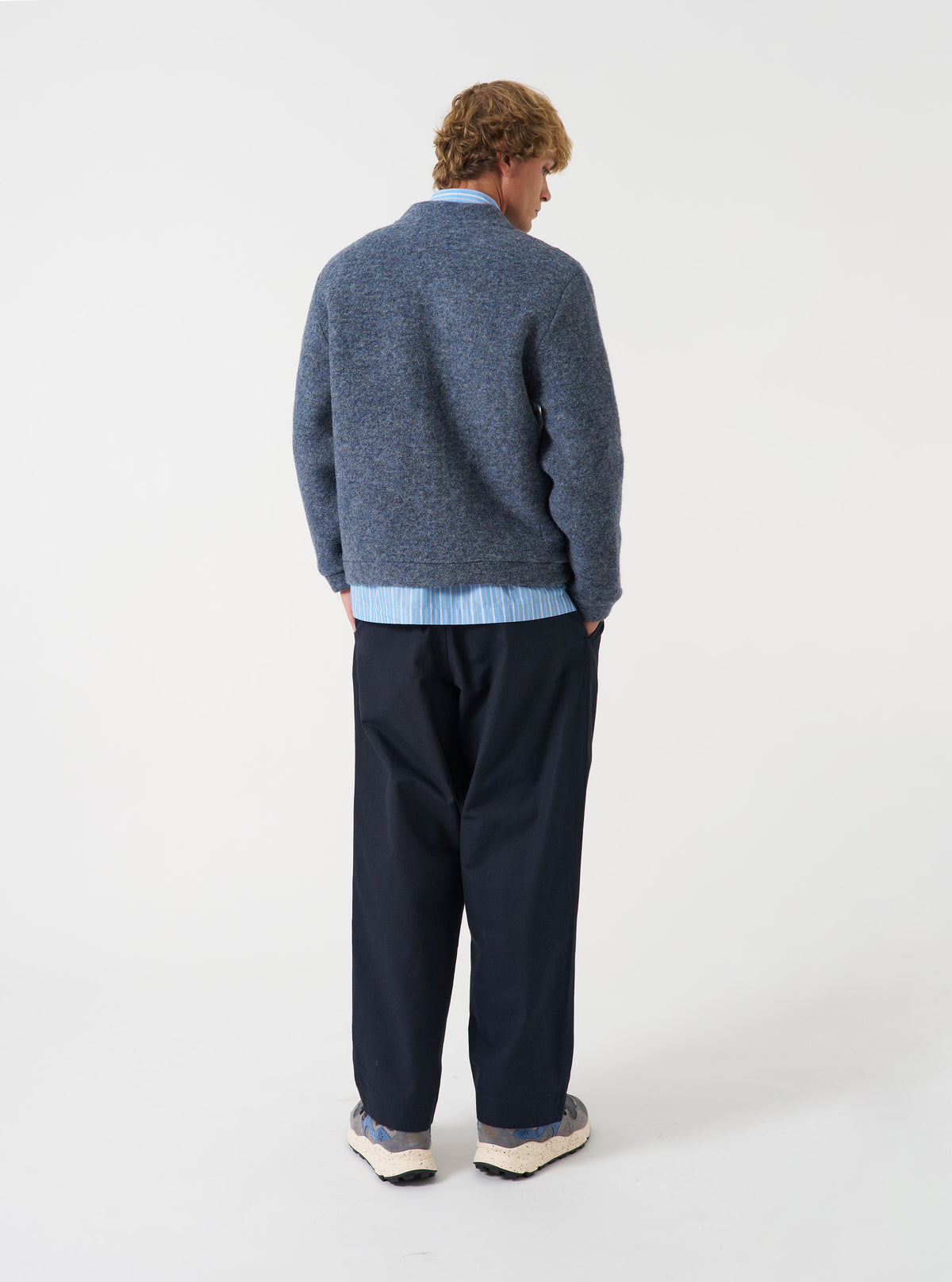 A model wearing the Slate Blue Wool Fleece Advance Cardigan shown from an alternate angle against a plain studio backdrop, highlighting the easy boxy silhouette and soft slate blue fleece fabric.