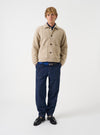 A male model wears the Fawn Wool Fleece Rams Jacket standing against a plain background. He wears the jacket buttoned up over casual trousers, showcasing its boxy cut, point collar, and large front pockets.