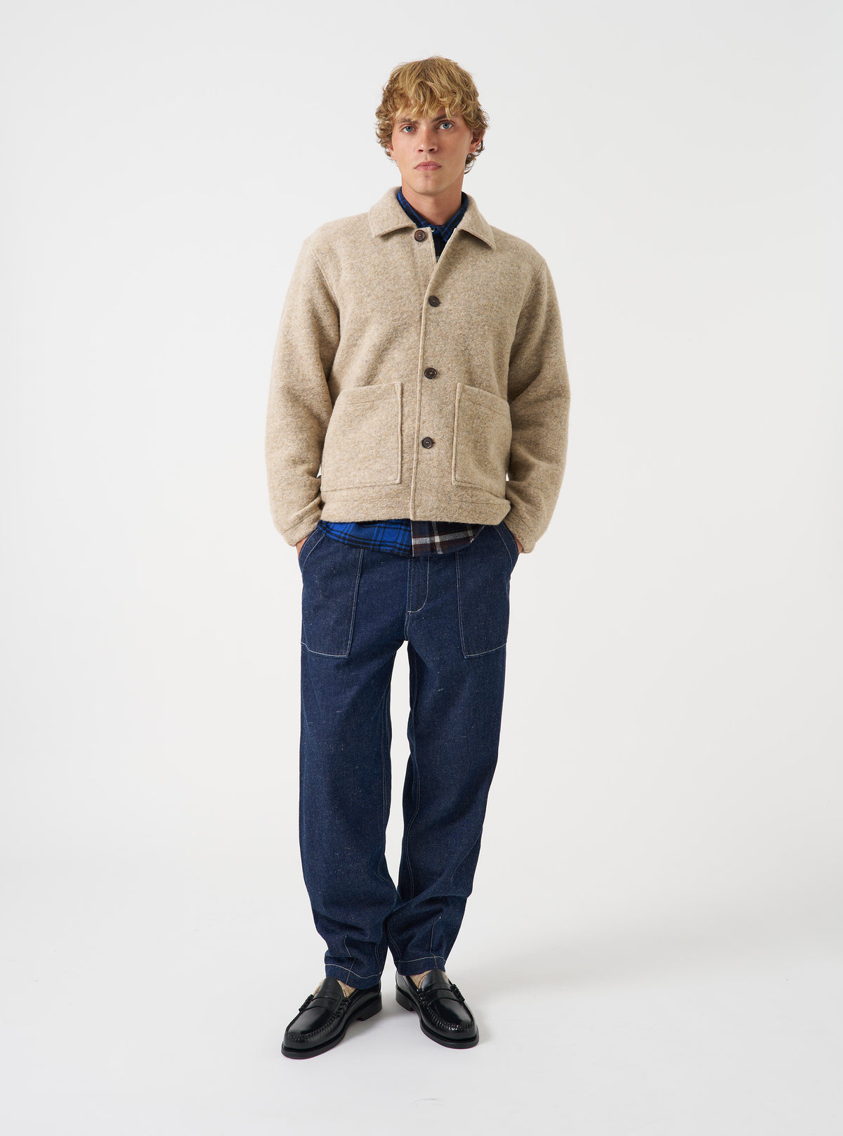 A male model wears the Fawn Wool Fleece Rams Jacket standing against a plain background. He wears the jacket buttoned up over casual trousers, showcasing its boxy cut, point collar, and large front pockets.