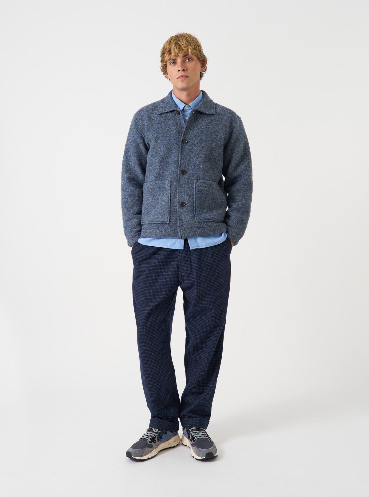 A male model wears the Slate Blue Wool Fleece Rams Jacket against a plain background. The jacket is styled open over a t-shirt, showing its casual boxy fit, dropped shoulders, and prominent patch pockets.