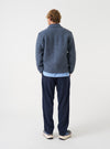 A male model wears the Slate Blue Wool Fleece Rams Jacket posed turned away from the camera against a neutral studio backdrop, highlighting the broad back fit, low shoulder seam, and relaxed drape.