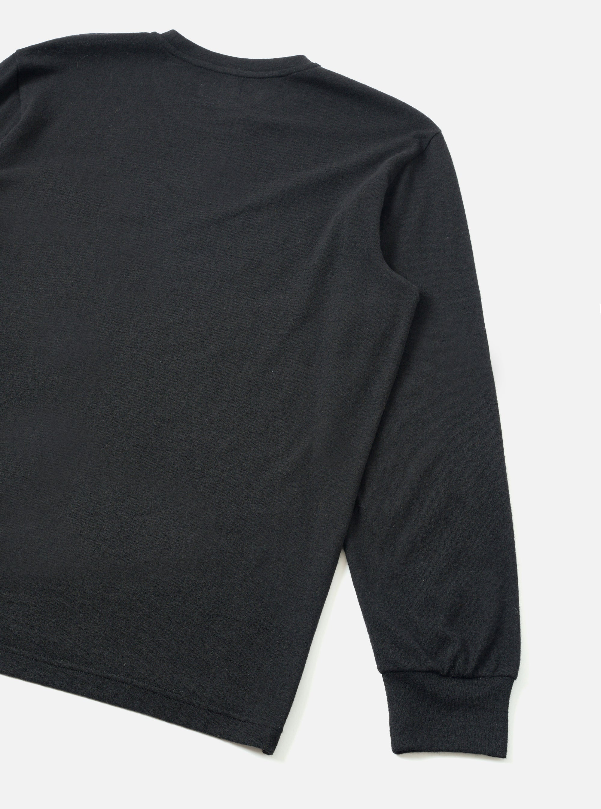 Black long-sleeve pocket tee in recycled wool mix fabric, shown as a flat lay on a white surface. The rear view shows the back panel, right shoulder seam, and full-length sleeve with a ribbed cuff at the wrist. A crew neckline is partially visible at the top. The fabric has a fine, lightly textured surface with a matte finish.
