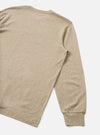 Flat lay of a dark sand long-sleeve pocket tee in a heathered wool-mix jersey fabric, shot on a light grey seamless backdrop. The back and right sleeve are visible, showing a ribbed cuff at the wrist and clean shoulder seam. No print or branding is visible from this angle.