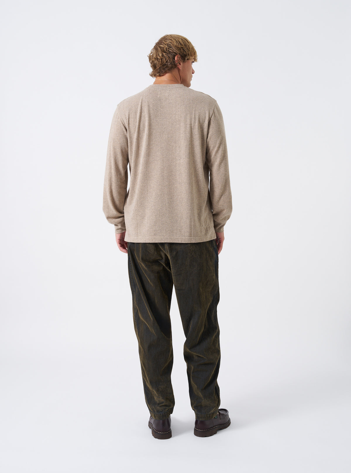 Studio view of a model wearing the Dark Sand Recycled Wool Mix SJ L/S Pocket Tee, showing the back and side profile with its relaxed silhouette, dropped rear hem, and cuffed long sleeves.