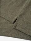 Close-up flat lay of an olive marl recycled wool mix long-sleeve pocket tee on a white surface. The shot focuses on the lower hem and cuff, showing a ribbed hem with overlock stitching, a folded ribbed cuff, and a small welt thumb loop detail. The heathered fabric has a soft, lightly textured finish.