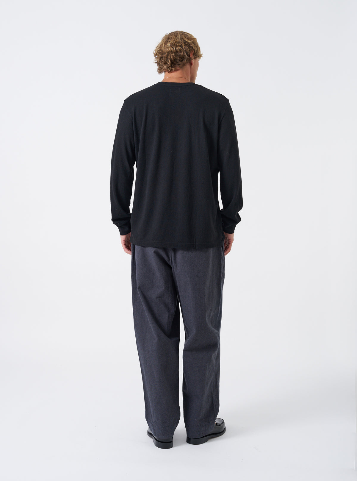 Alternate view of a model wearing the Black Recycled Wool Mix SJ L/S Pocket Tee in a studio setting. The long-sleeve tee showcases a comfortable fit, ribbed crew collar, and front chest patch pocket.